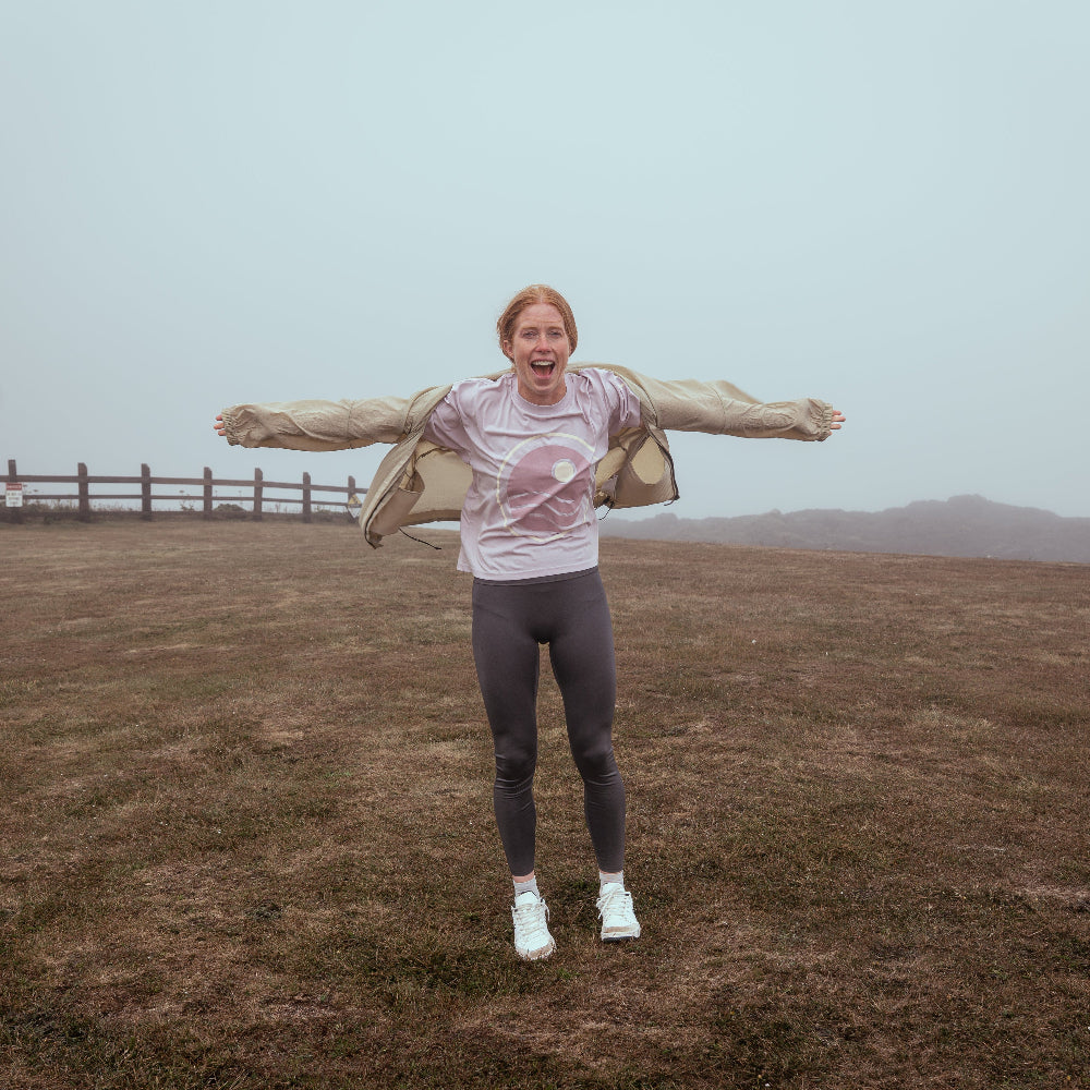Person standing in a field with arms outstretched on a foggy day
