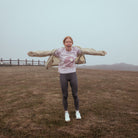 Person standing in a field with arms outstretched on a foggy day