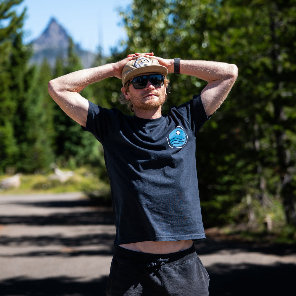 Person wearing sunglasses and a cap with a scenic background of trees and mountains.