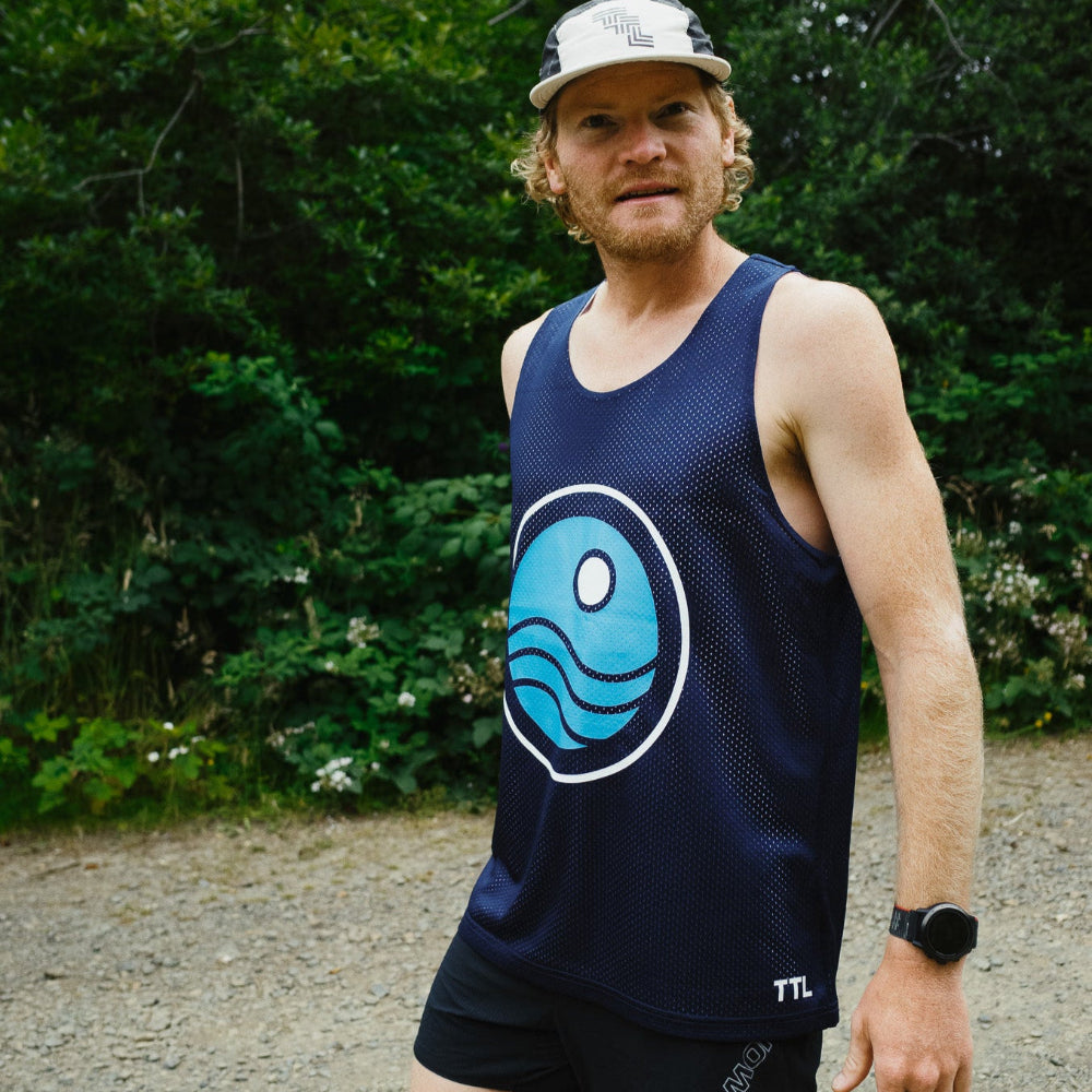 Man wearing a navy tank top with a blue logo and black shorts outdoors.