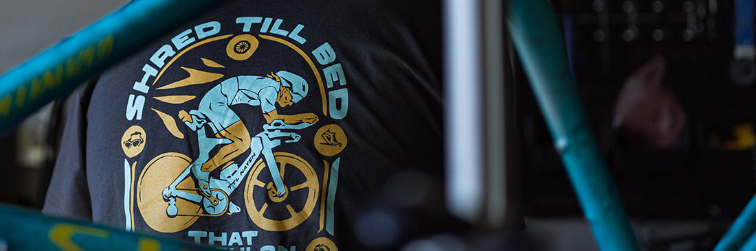 The back of the That Triathlon Life Shred til Bed tee shirt, looking through the frame of a blue speckled Specialized tarmac